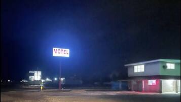 Un motel con un llamativo letrero que dice 'MOTEL', un estacionamiento de grava y un edificio de fachada verde y blanca.