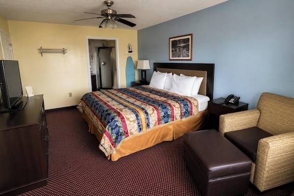 A hotel room with a bed, a desk, a chair, a telephone, and a ceiling fan.