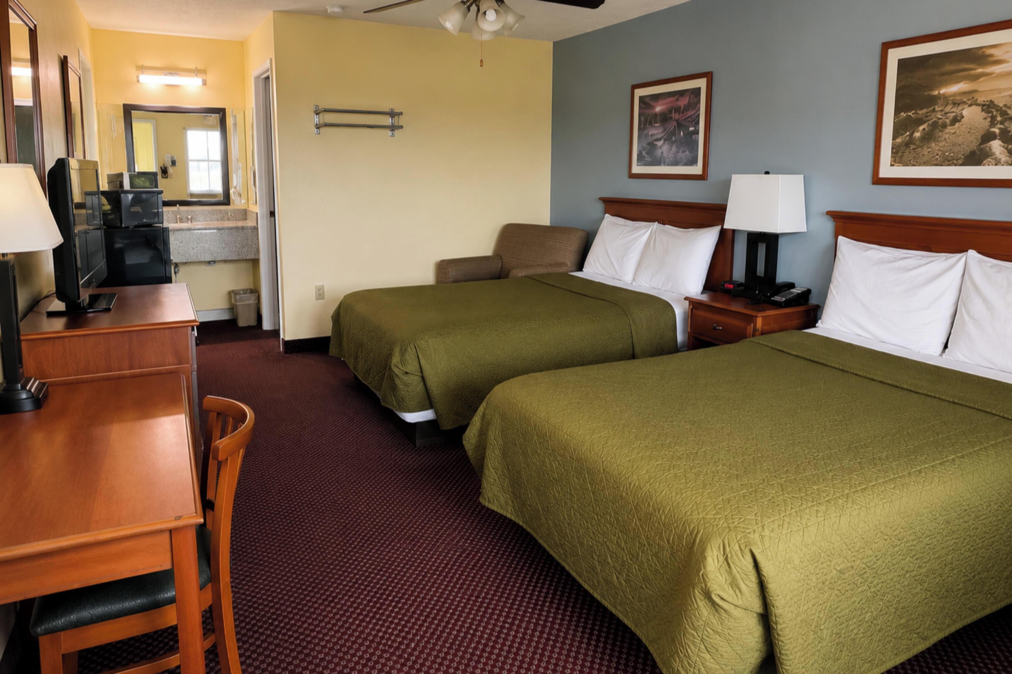 A hotel room with two beds, a desk, a chair, a TV, and a bathroom.