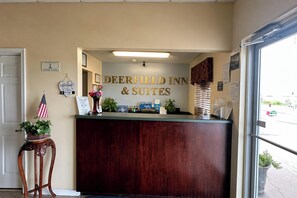 Un mostrador de recepción en Deerfield Inn & Suites con detalles de madera, un letrero de bienvenida y una pequeña bandera estadounidense.