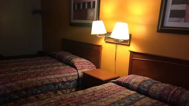 A hotel room with two beds, a nightstand, and two wall-mounted lamps. - Townhouse Motor Lodge Springfield Oh (Springfield)