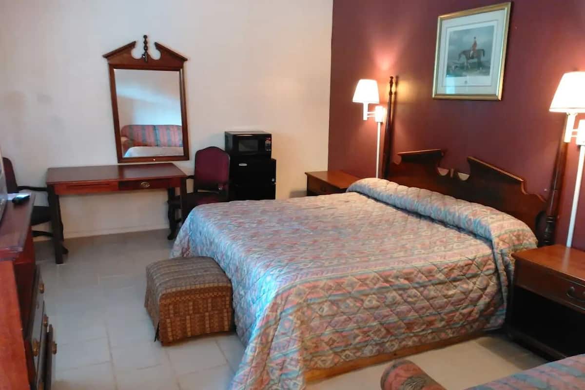 A bedroom with a bed, a desk, a chair, a dresser, and a lamp.
