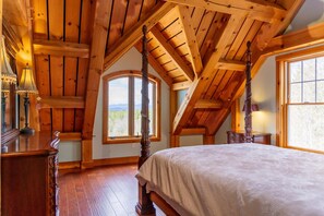 A bedroom with a wooden ceiling, a large bed, a window with a view, and a lamp. - Luxury Mountain Estate | Spectacular Views (Sweden)