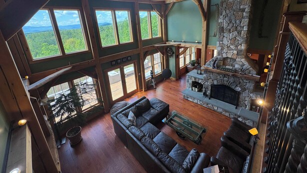 A spacious interior with a stone fireplace, large windows offering a view of the outdoors, and a wooden ceiling structure. - Luxury Mountain Estate | Spectacular Views (Sweden)