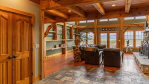 A spacious living area with a stone floor, wooden ceiling beams, a fireplace, and a large window offering a view of the outdoors. - Luxury Mountain Estate | Spectacular Views (Sweden)