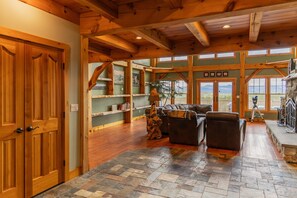 A spacious living area with a stone floor, wooden ceiling beams, a fireplace, and a large window offering a view of the outdoors. - Luxury Mountain Estate | Spectacular Views (Sweden)