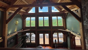 A high-ceilinged room with large windows, wooden beams, and a view of a forested landscape. - Luxury Mountain Estate | Spectacular Views (Sweden)