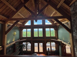 A high-ceilinged room with large windows, wooden beams, and a view of a forested landscape. - Luxury Mountain Estate | Spectacular Views (Sweden)