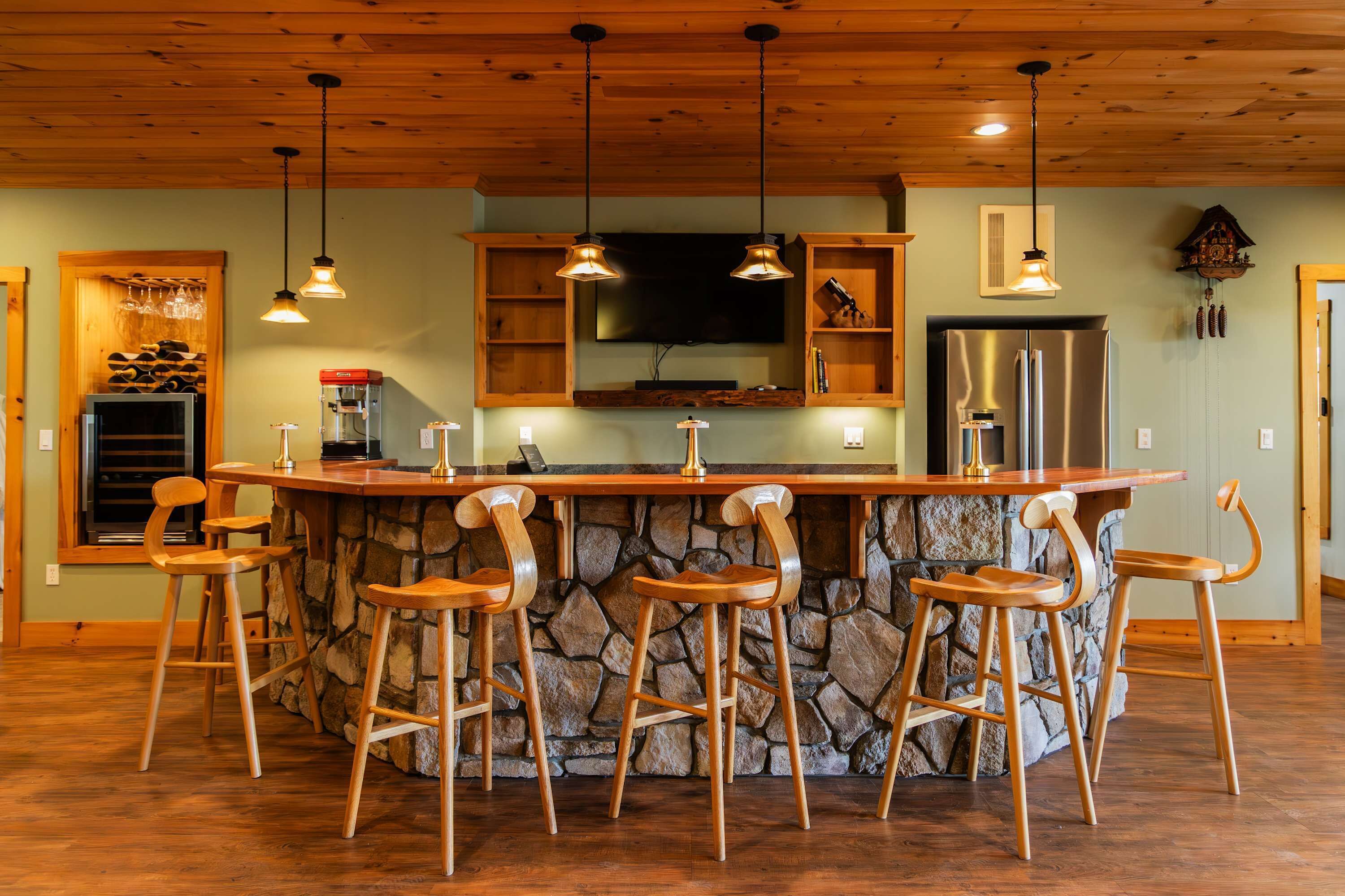 Une cuisine dotée d’un îlot central, de tabourets de bar, de meubles en bois, d’un réfrigérateur et de luminaires suspendus.