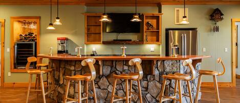 Une cuisine dotée d’un îlot central, de tabourets de bar, de meubles en bois, d’un réfrigérateur et de luminaires suspendus.