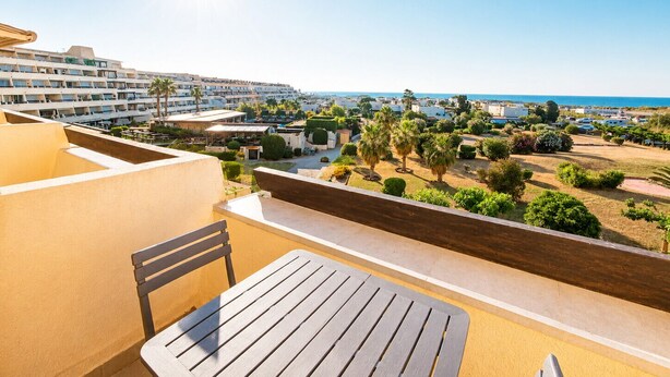 A balcony with a table and chair, overlooking a resort area with buildings and a view of the sea. - Naturiste Cap d'Agde Port Nature 740 (Agde)