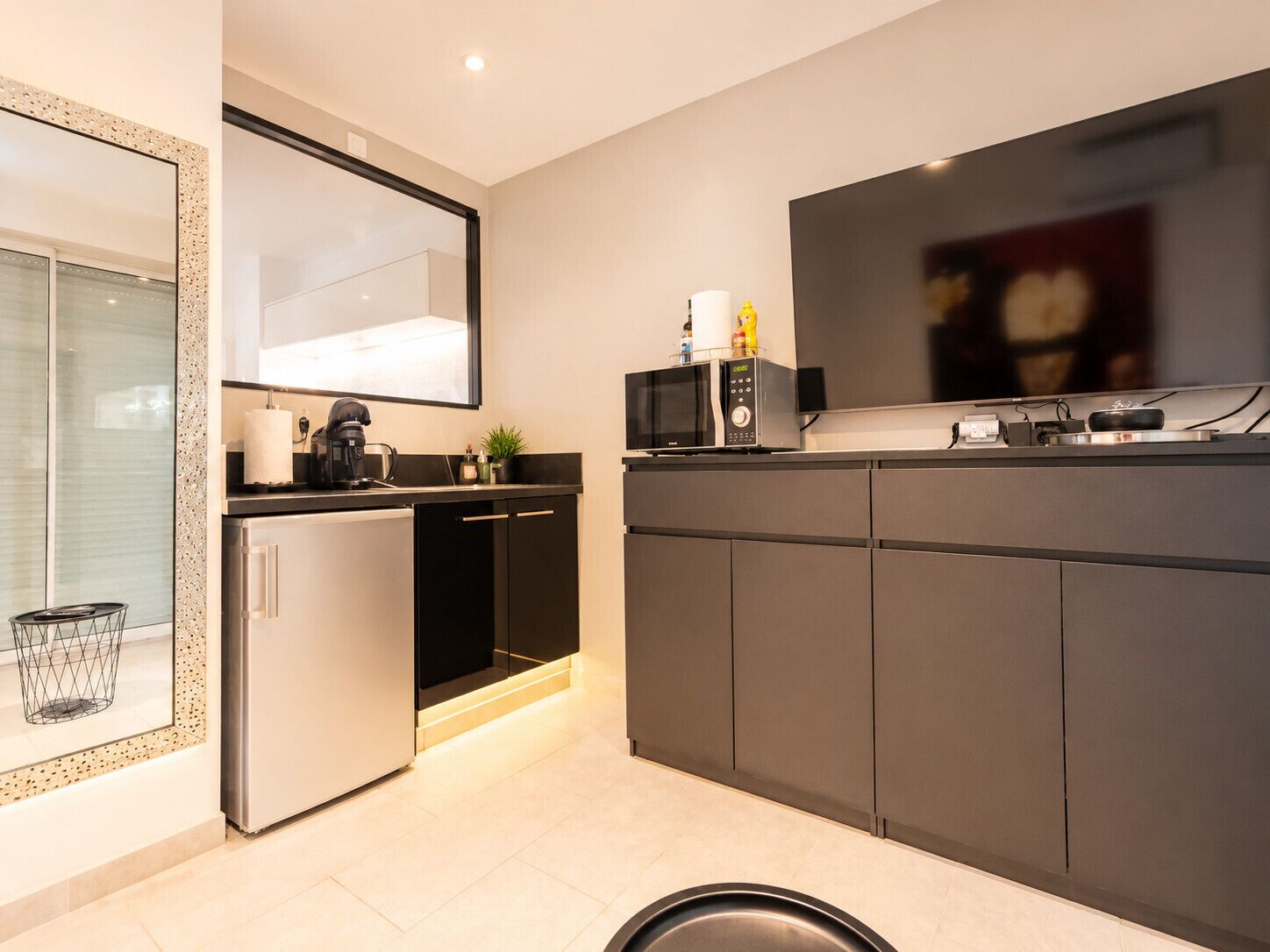 Een moderne keuken met een ingebouwde magnetron, koffieapparaat en een flatscreen televisie.
