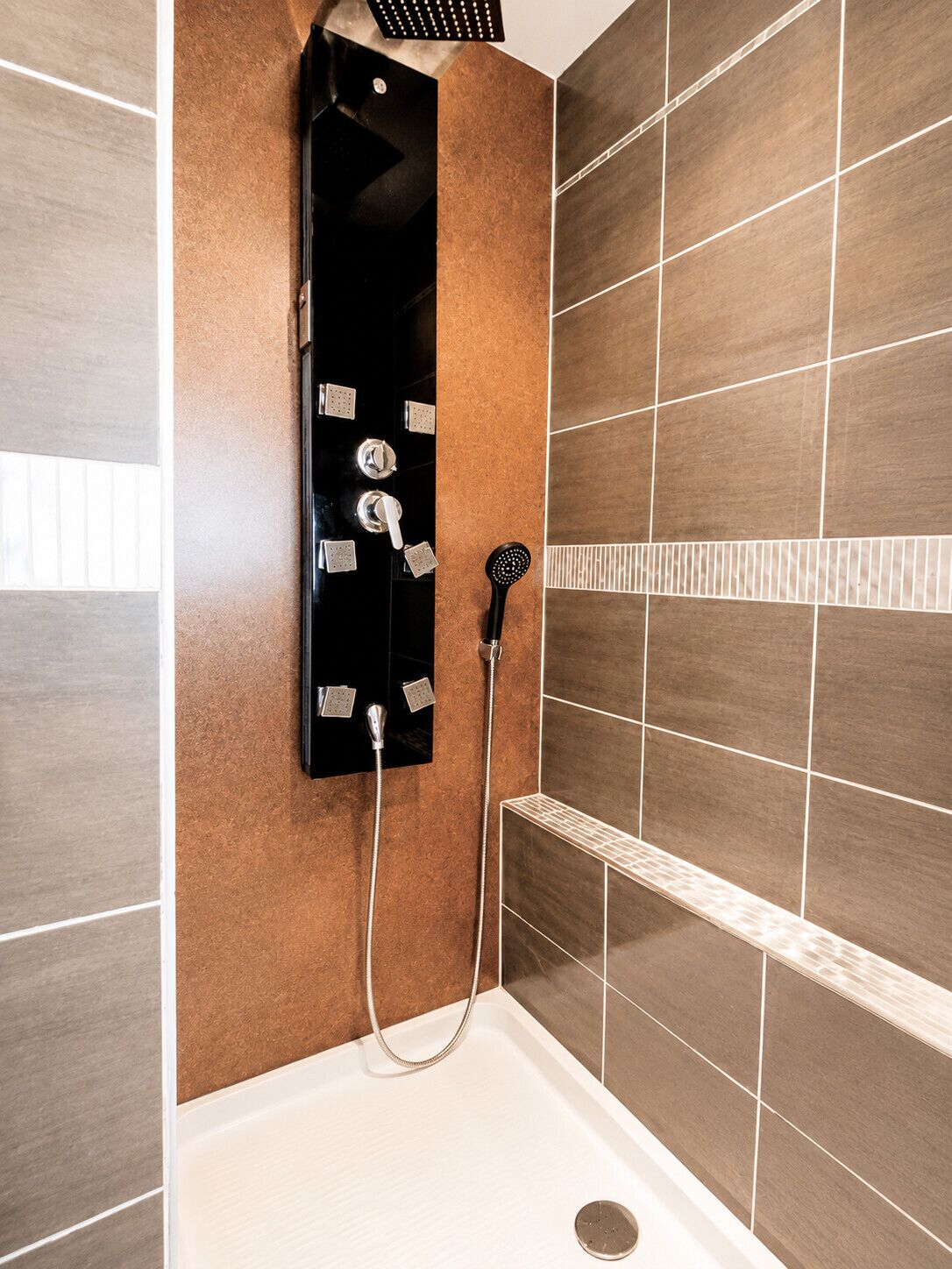 Un baño moderno con ducha integrada, cabezal de ducha de mano y grifo empotrado en la pared.