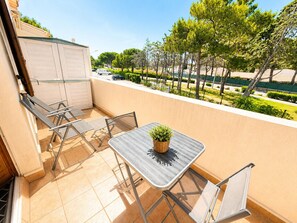 Ein Balkon mit Tisch und Stühlen, einem Blumentopf und Blick auf ein Wohngebiet mit Bäumen und parkenden Autos.