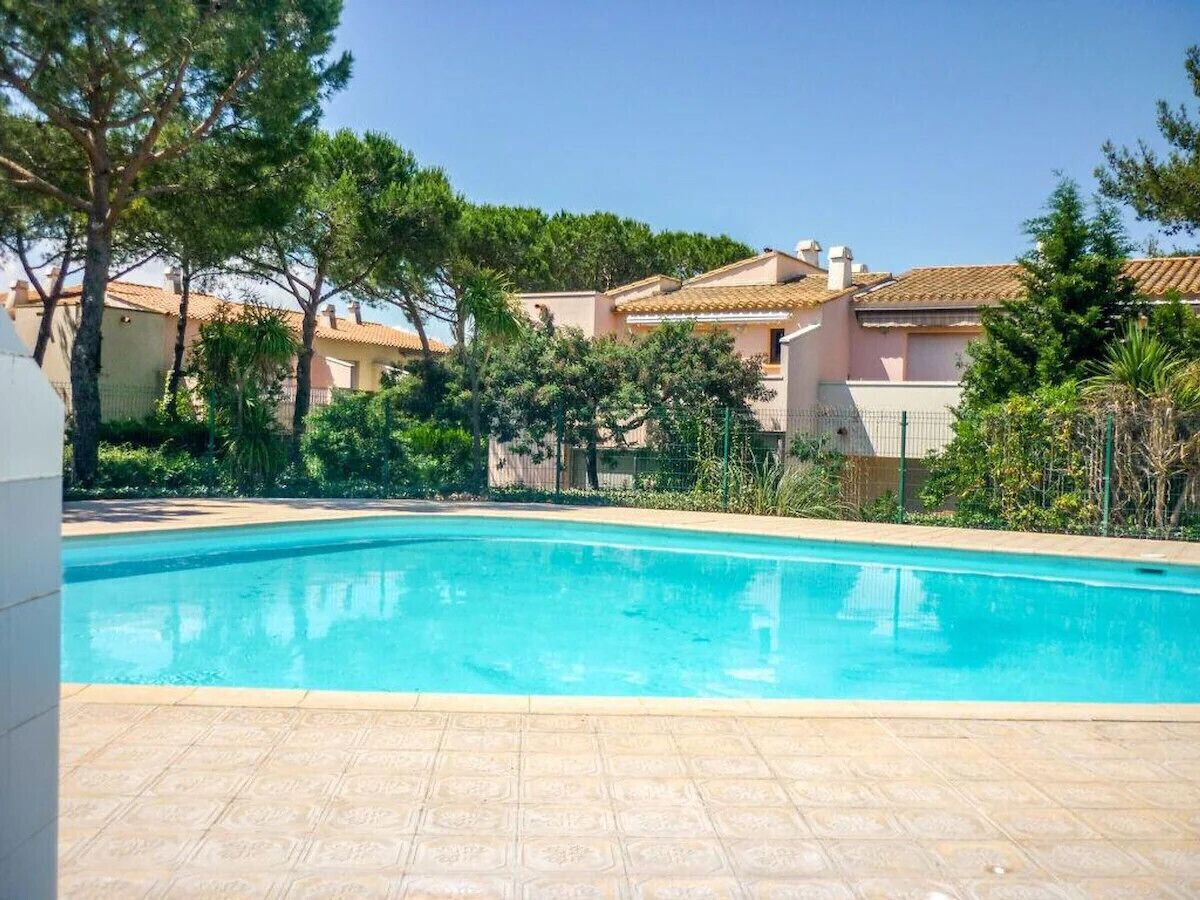 A swimming pool with a tiled deck, surrounded by greenery and buildings with terracotta roofs.
