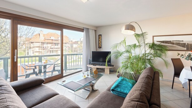 Un soggiorno moderno con divano, tavolino in vetro, televisore e balcone con vista sugli edifici.
