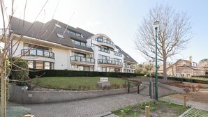 Un moderno edificio residenziale con balconi, una strada privata pavimentata e un cartello che indica un campo da golf nelle vicinanze.