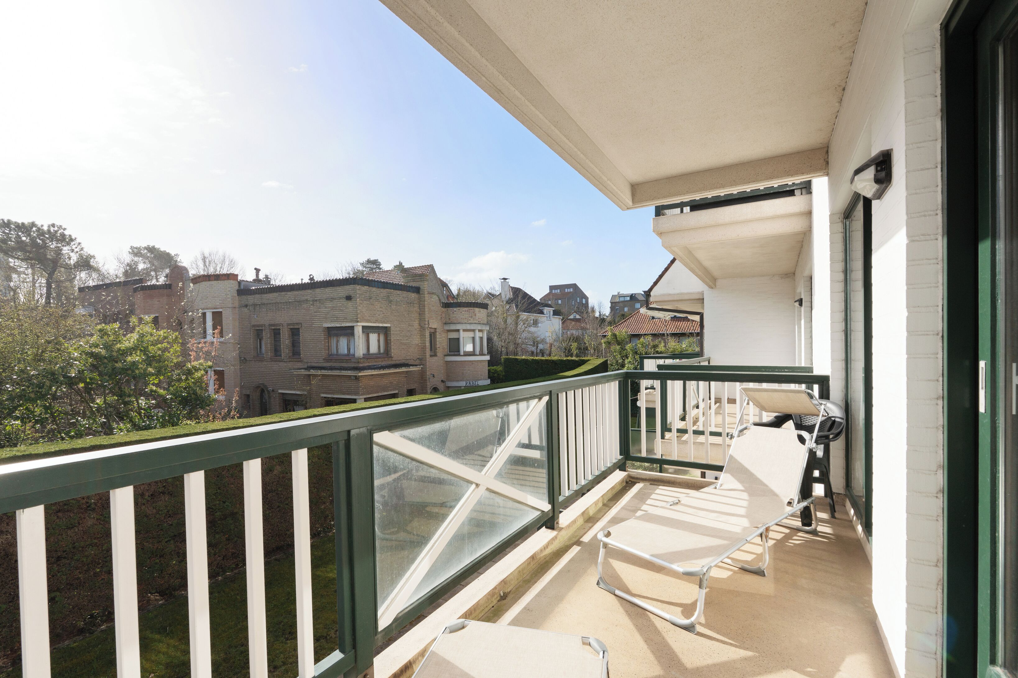 A balcony with a view of residential buildings, a white chair, and a table.
