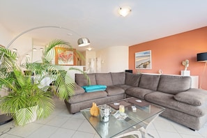 Ein modernes Wohnzimmer mit einem Ecksofa, einem Glastisch und einer großen Topfpflanze.