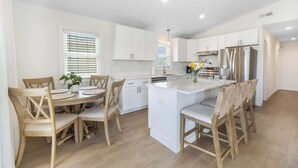 Une cuisine moderne avec des meubles blancs, un îlot central et un coin repas comprenant des chaises et une table en bois.