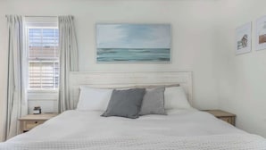 Une chambre à coucher avec un lit, une table de chevet, une fenêtre avec des rideaux et un tableau au mur.