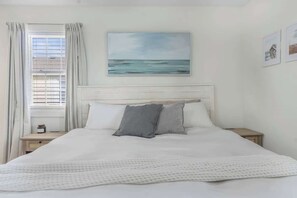 Ein Schlafzimmer mit einem Bett, einem Nachttisch, einem Fenster mit Vorhängen und einem Gemälde an der Wand.