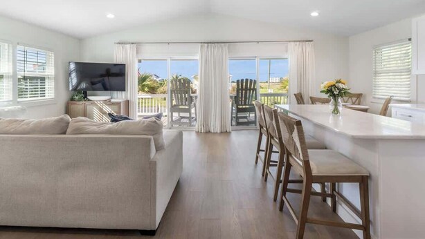 Un vaste espace de vie comprenant un canapé, un téléviseur, un coin repas avec des chaises et une table, ainsi qu’un ventilateur de plafond.