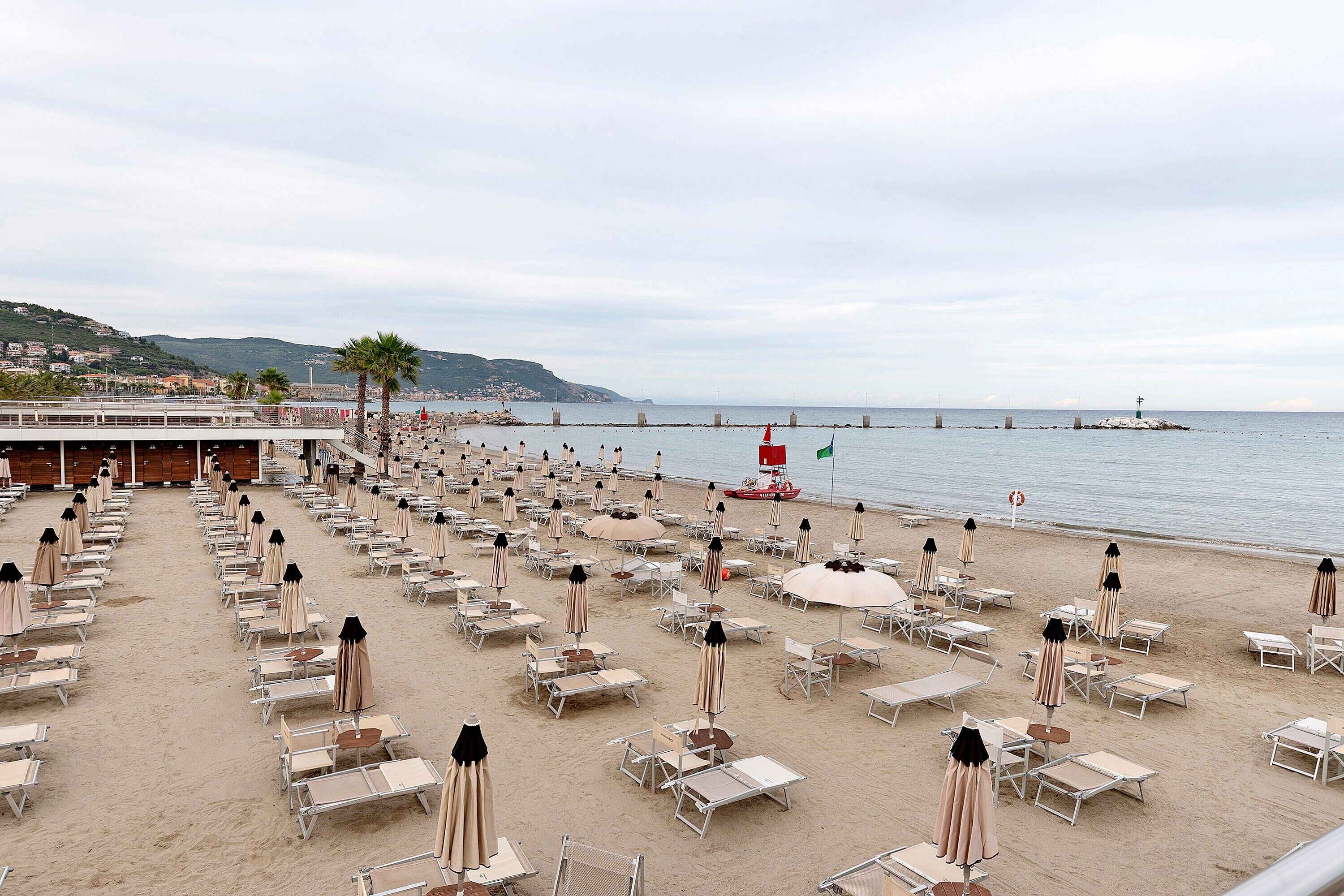 A beach with rows of sun loungers and umbrellas, a pier extending into the sea, and a hill with buildings in the background.. Apartment 'M&M House Beach - 4 Salti Dal Mare' with Mountain View, Wi-Fi and Air Conditioning