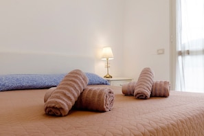 Una cama bien hecha con toallas enrolladas, una lámpara de noche y un cojín estampado.