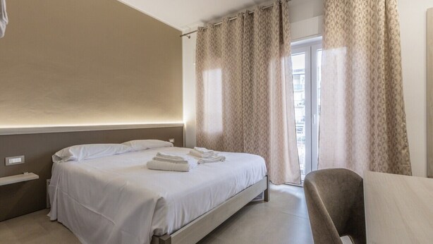 Une chambre d’hôtel avec un lit, une chaise, une table de chevet et une fenêtre avec des rideaux.