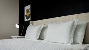 A neatly made bed with white bedding, a bedside lamp, and a framed picture on the wall.