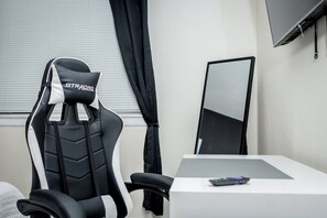 Una habitación moderna con una butaca de estilo carreras, un televisor de pantalla plana en la pared y una mesa con un control remoto.