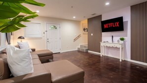 A modern living room with a sofa, a coffee table, a TV mounted on the wall, and a staircase leading to another level.