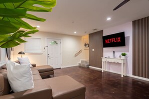 Una sala de estar moderna con un sofá, una mesa de centro, un televisor montado en la pared y una escalera que sube a otro nivel.
