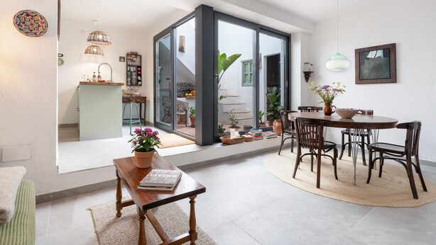 Un espace de vie à aire ouverte comprenant une table à manger, des chaises, un canapé et une cuisine visible à travers une porte vitrée.