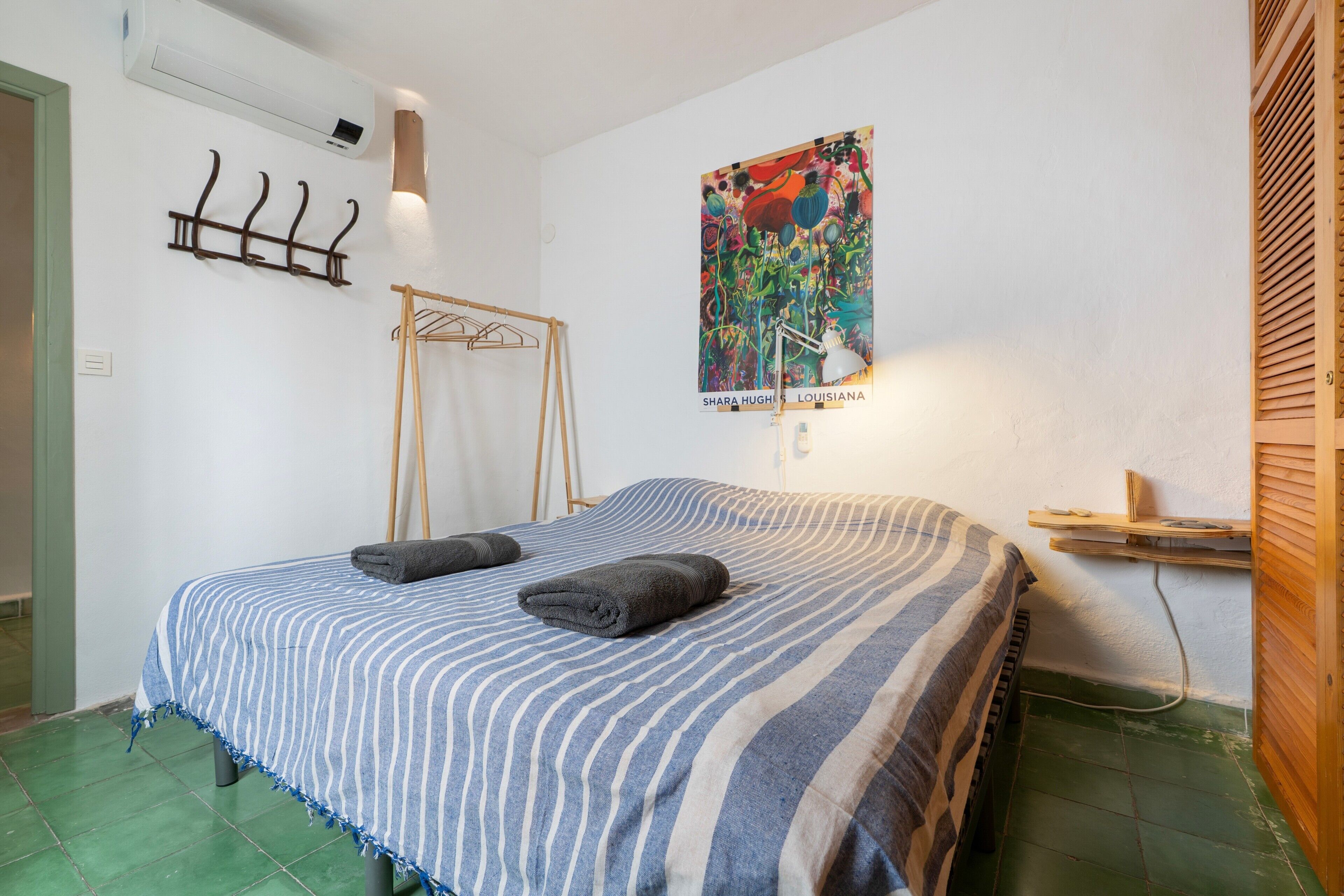 Un dormitorio con edredón a rayas, una lámpara de pared, un cartel y un estante de madera.
