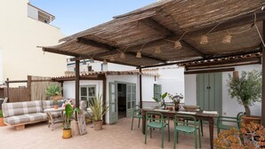 Une terrasse couverte avec un canapé, une table à manger, des chaises et des plantes en pot.