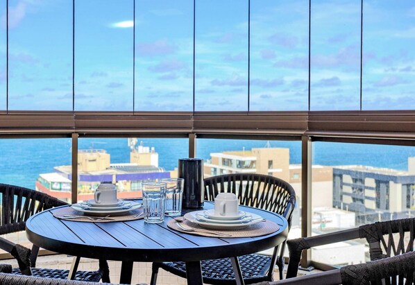 Ein runder Tisch mit Blick auf das Meer und Gebäude, gedeckt mit Tellern, Gläsern und einer Tasse.
