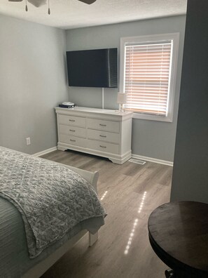 Ein Schlafzimmer mit Bett, Schminktisch und einem an der Wand befestigten Fernseher.