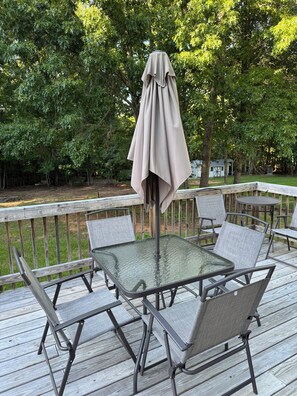 Eine Terrasse mit einem Glastisch und vier Stühlen, umgeben von einem Holzdeck und einem Sonnenschirm.