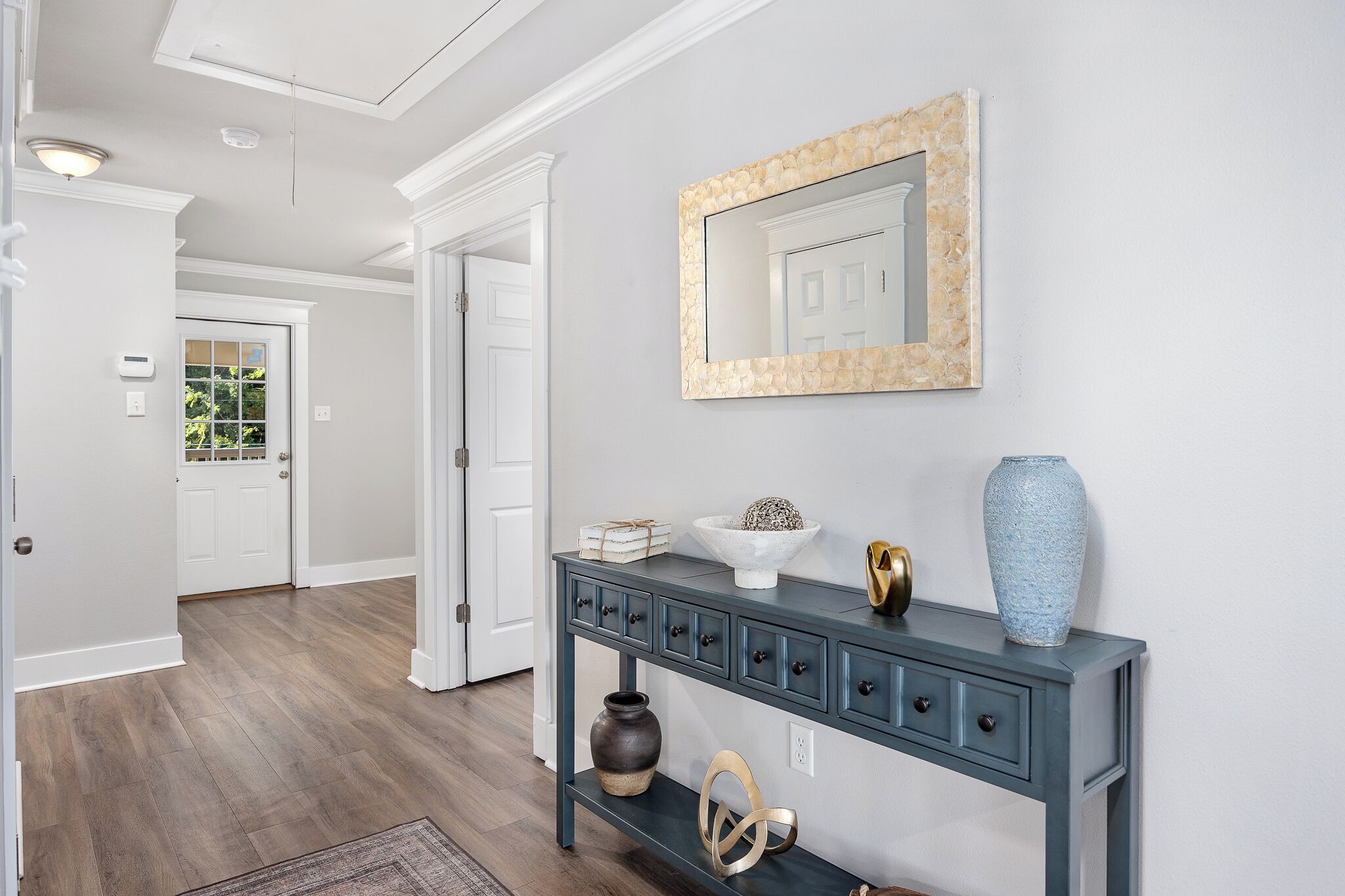 A hallway with a dark blue console table, a mirror, and decorative items.
