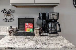 A kitchen counter with a coffee maker, coffee mugs, a coffee grinder, and a coffee-themed wall decoration. - Garden District Luxury Oasis-Private Garage (Baton Rouge)