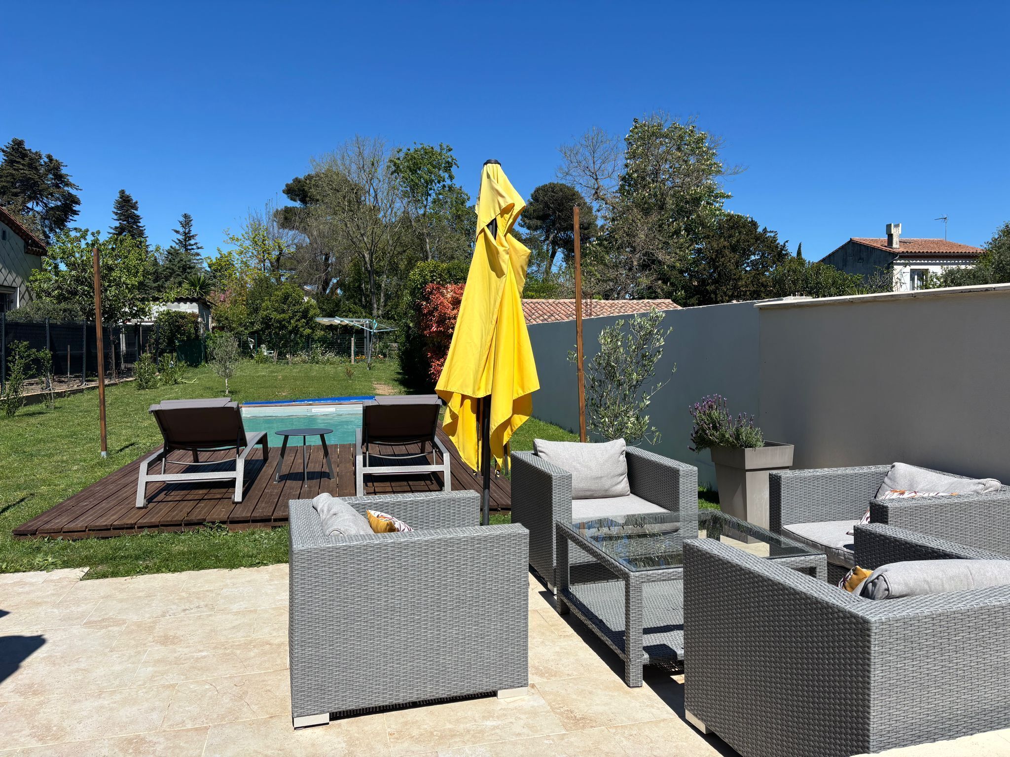 An outdoor patio with wicker furniture, a yellow umbrella, and a swimming pool in the background.