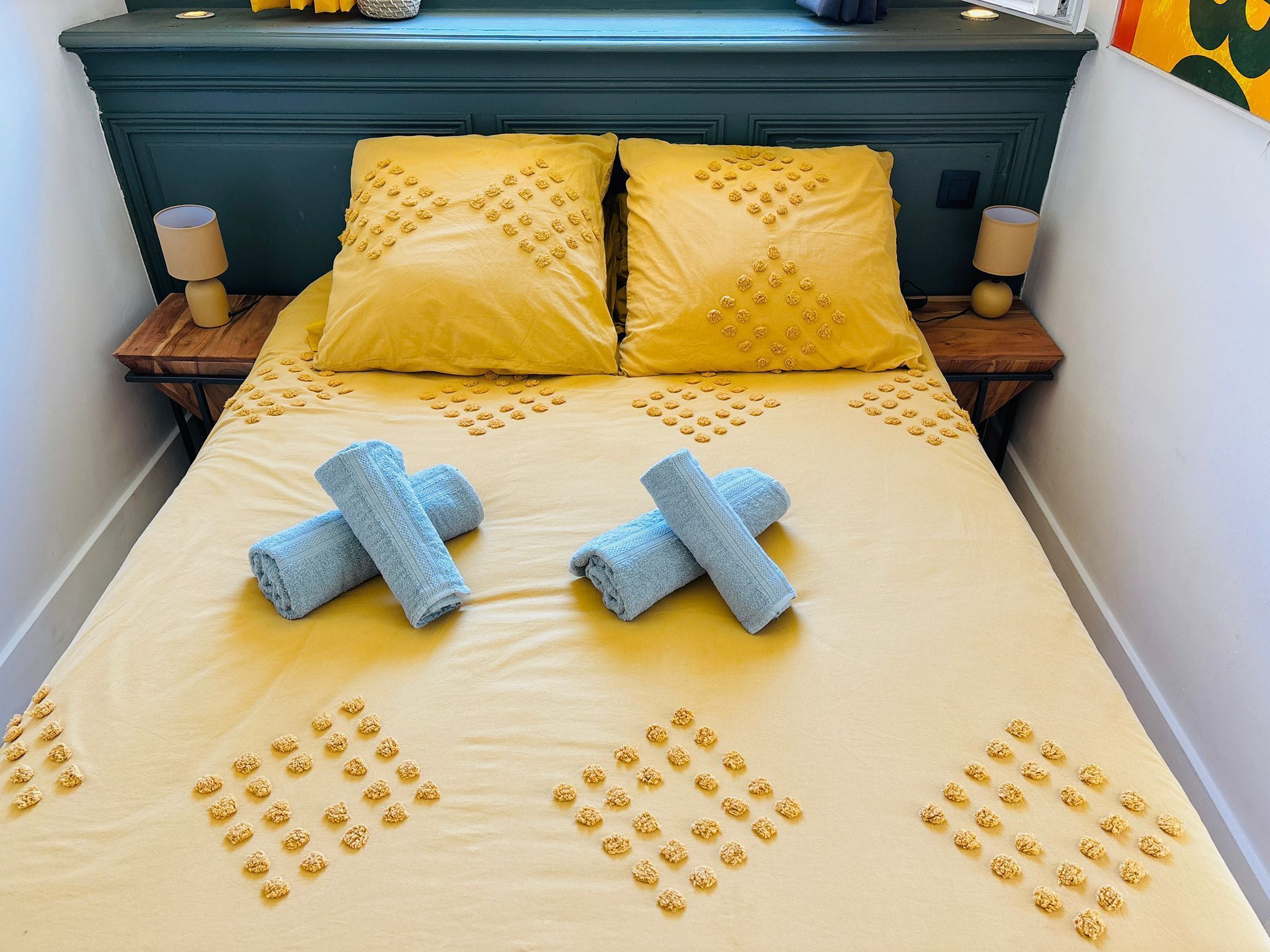 Ein Bett mit gelben Kissen, zwei blauen Handtüchern und goldenen Verzierungen auf der Bettdecke.