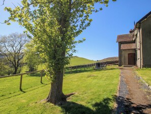 A rural landscape with a large tree, a building with a red door, and a fenced area. - Beach Farmhouse (Bishops Castle)