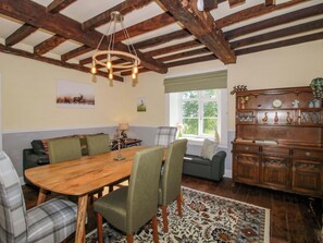 A dining area with a wooden table, chairs, a chandelier, a sofa, and a cabinet with decorative items. - Beach Farmhouse (Bishops Castle)