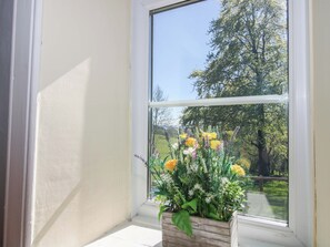A window with a view of a green landscape and a flower arrangement. - Beach Farmhouse (Bishops Castle)