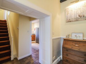 A hallway with a wooden staircase, a kitchen in the background, and a wooden dresser with a welcome sign. - Beach Farmhouse (Bishops Castle)