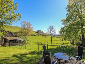 A patio with a table and chairs overlooking a green field and a stone building. - Beach Farmhouse (Bishops Castle)