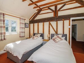 Ein Zimmer mit zwei Betten, Holzbalken an der Decke, einem Fenster mit Vorhängen und einer Tür zu einem anderen Raum.